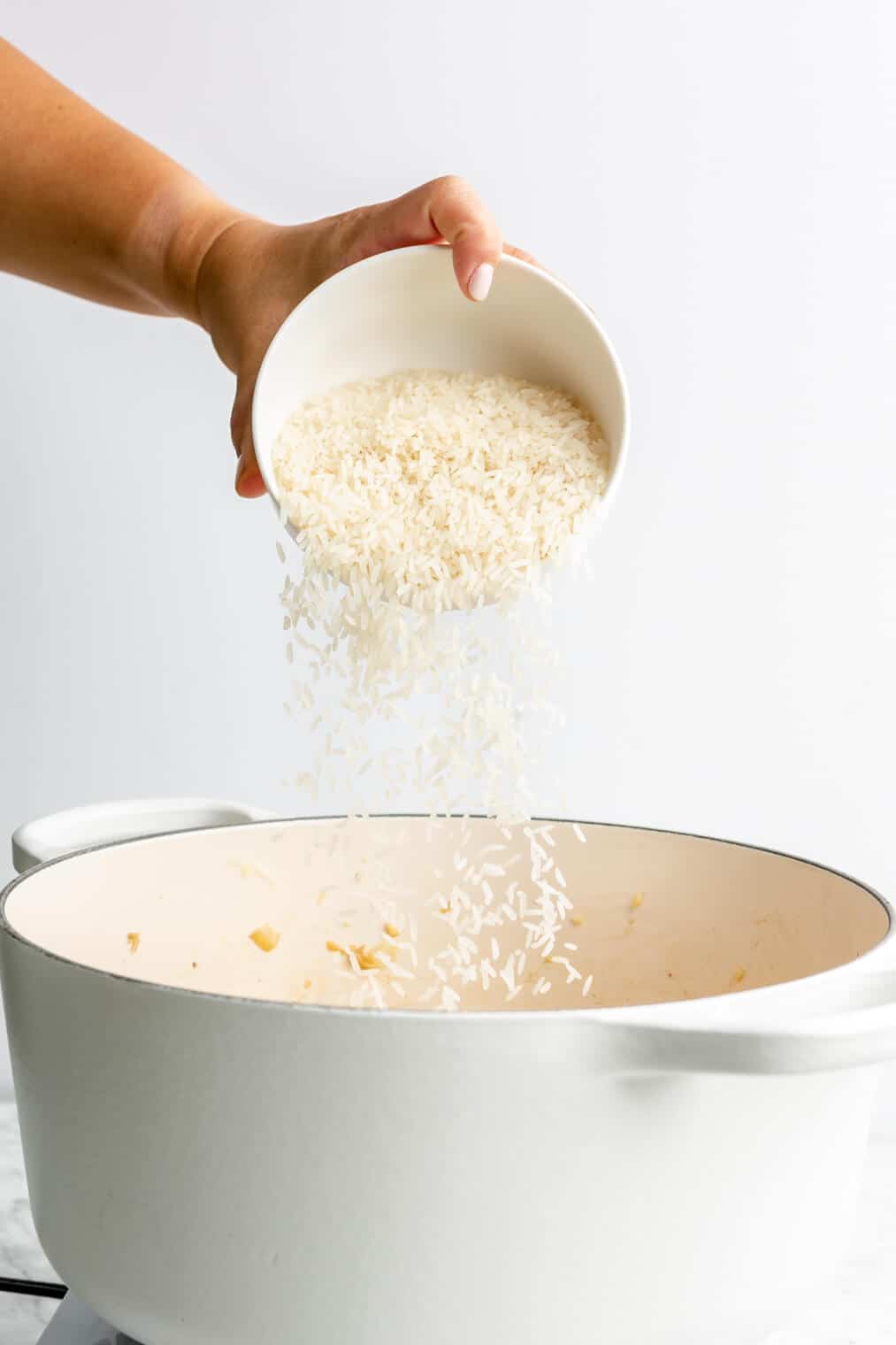 Rice being poured into a white dutch oven.
