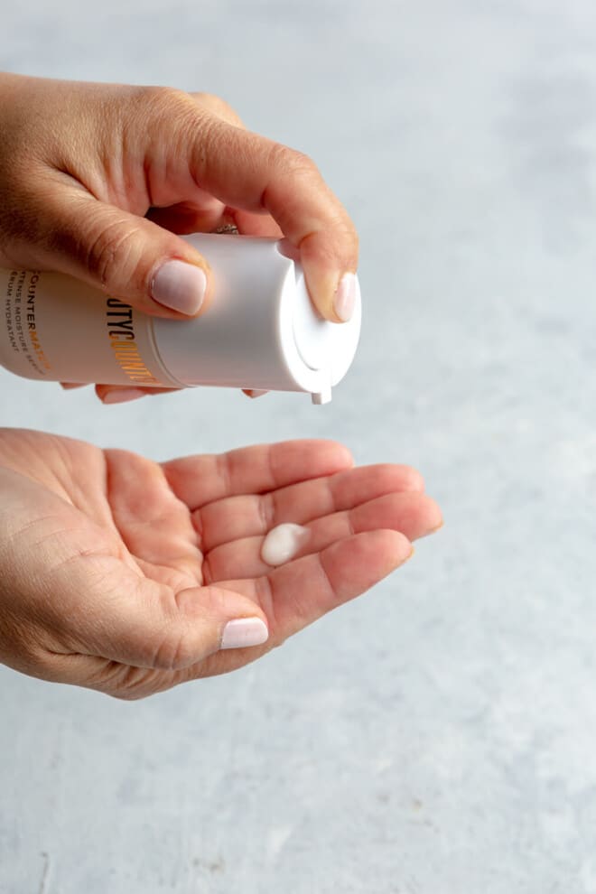 Pump of Countermatch serum on the fingertips of a hand. The other hand is holding the countermarch serum jar. 