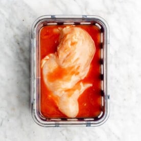 Chicken breast marinated in buffalo sauce in a glass container.