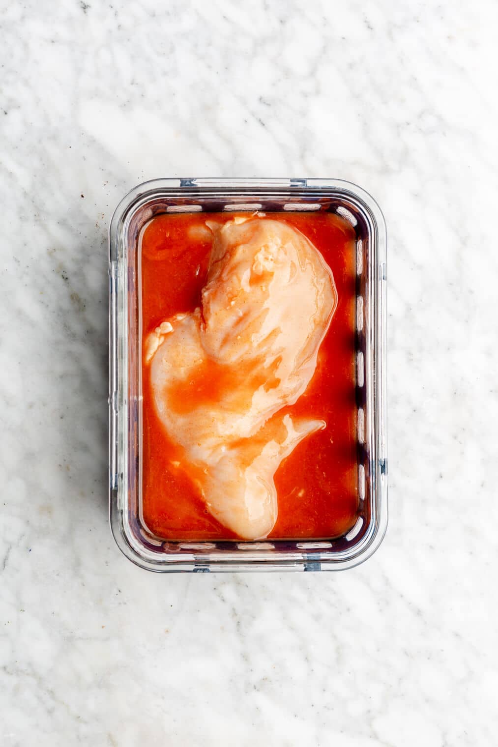 Chicken breast marinated in buffalo sauce in a glass container.