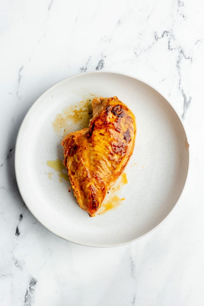 Pan seared buffalo chicken breast on a round plate on a grey and white marble surface. 