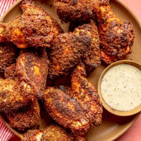 Brown plate with dry rubbed chicken wings served next to a side of ranch dressing.