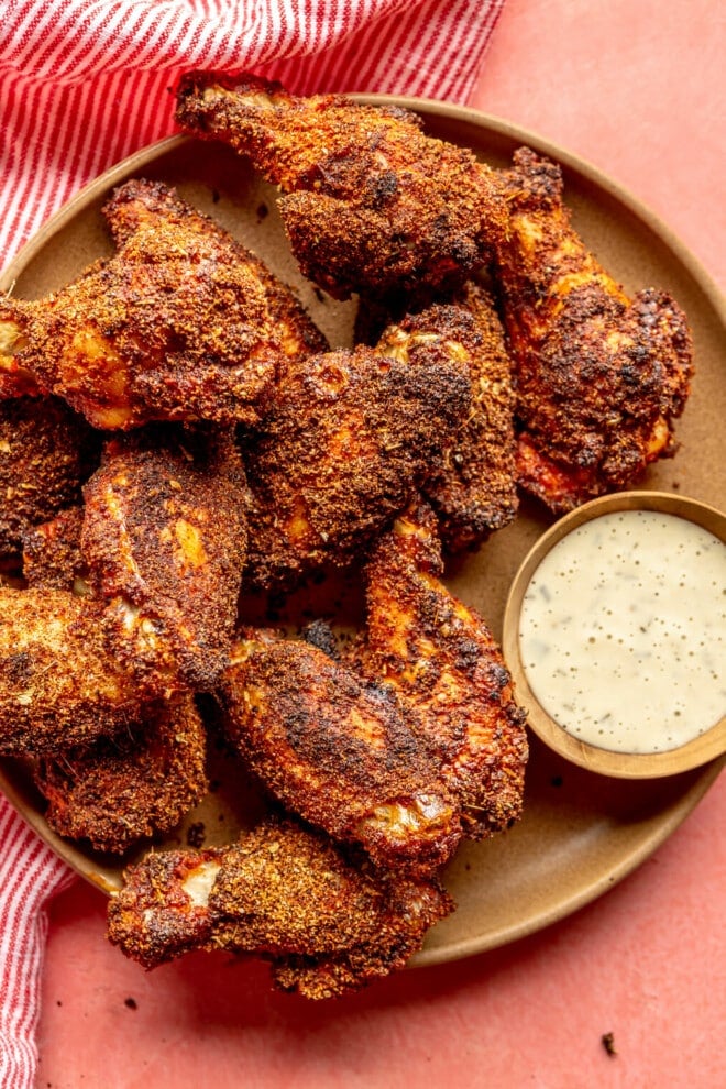 Brown plate with dry rubbed chicken wings served next to a side of ranch dressing.