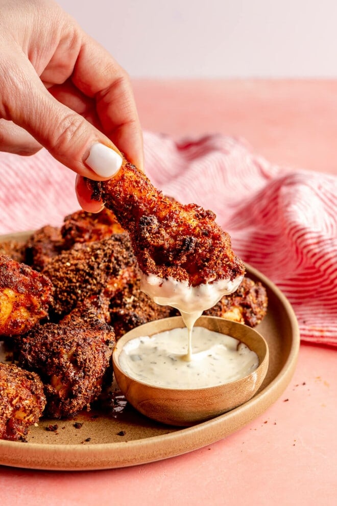 Hand holding a dry rub chicken wing dipped in ranch dressing.