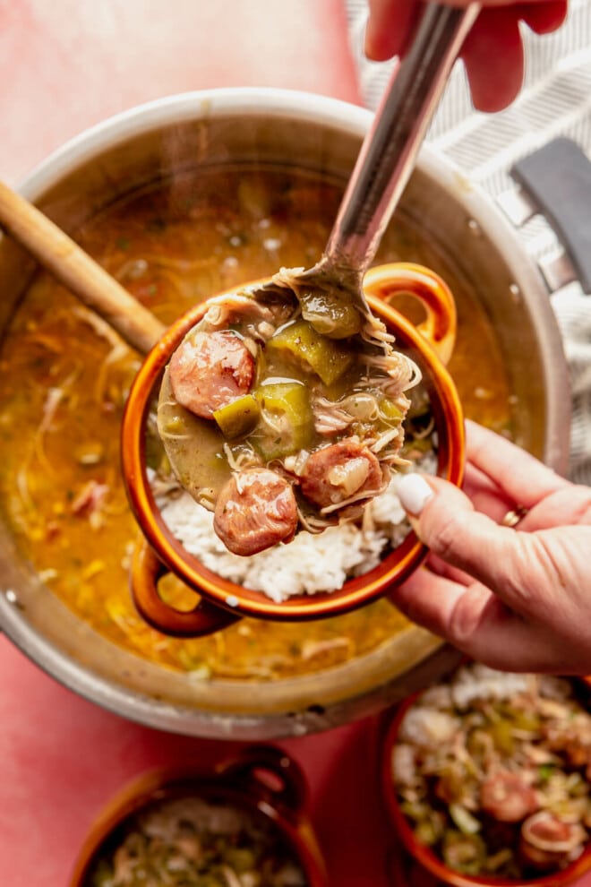 Hand scooping a serving of gumbo into a bowl with white rice.