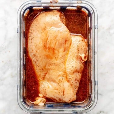 Chicken breast in a glass container with marinade.