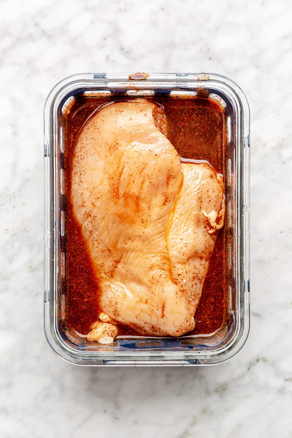 Chicken breast in a glass container with marinade.