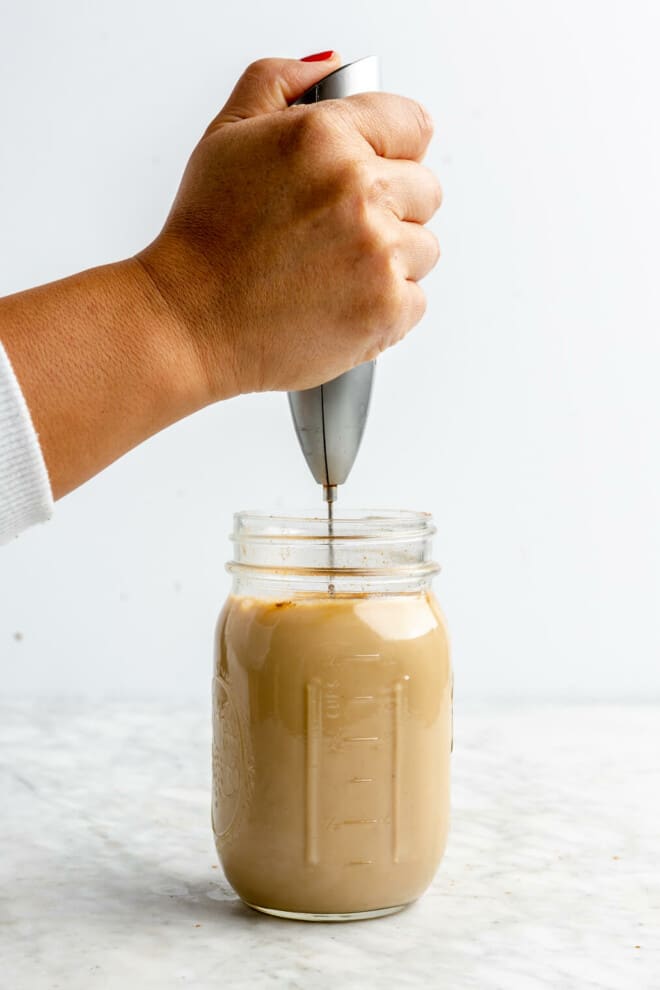 Hand holding frother inserted into a mason jar of coffee.