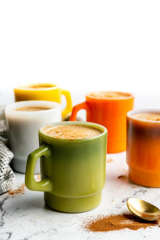 5 different colored coffee mugs with mushroom coffee in each one. 