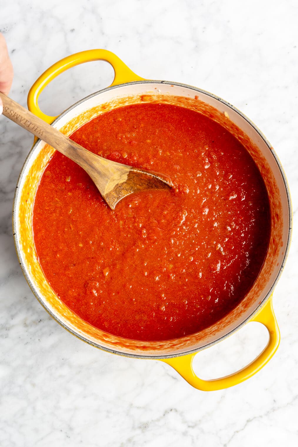 A red sauce in a yellow dutch oven with a wooden spoon.