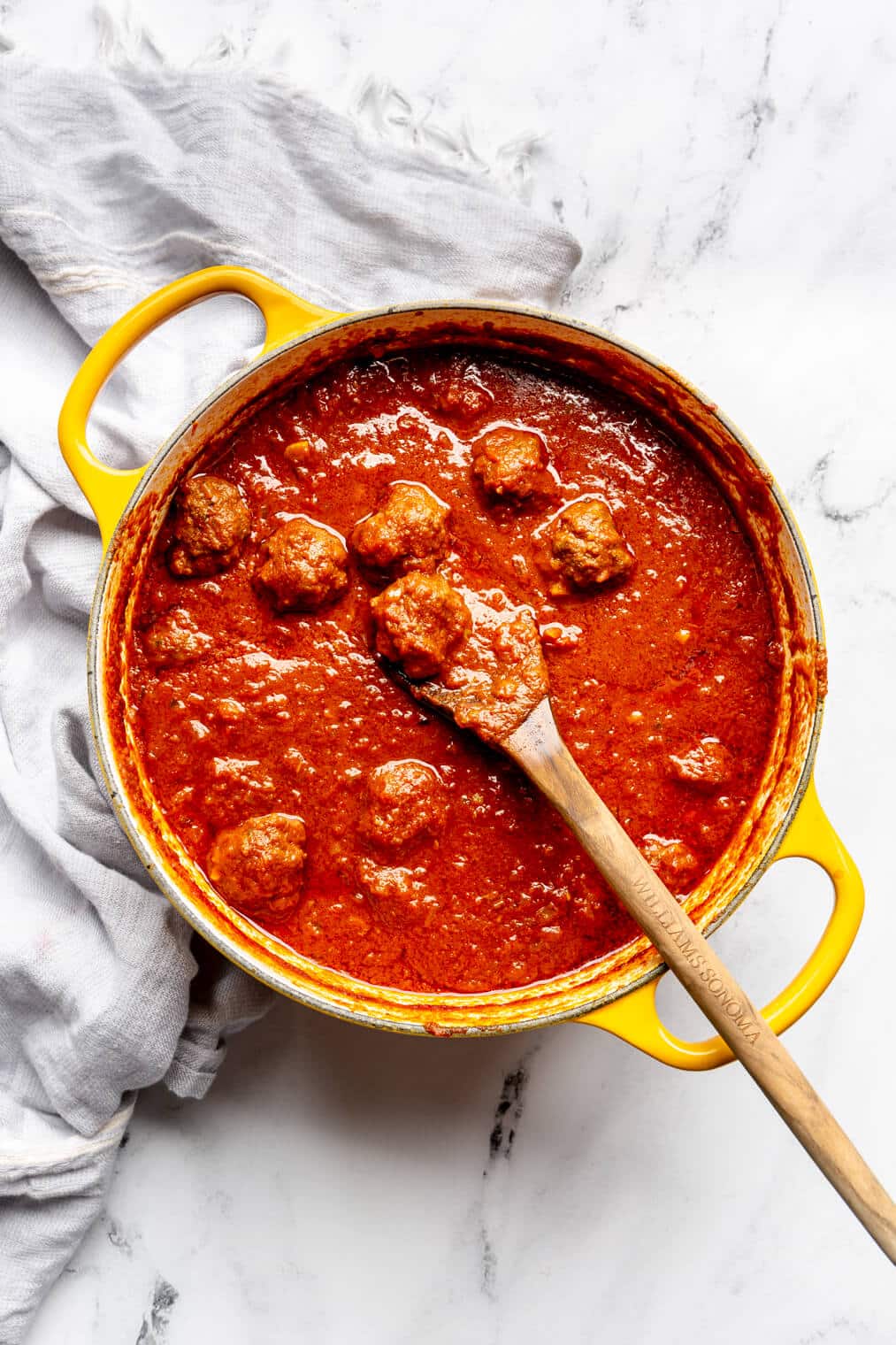 Cooked meatballs in a red sauce in a yellow dutch oven.