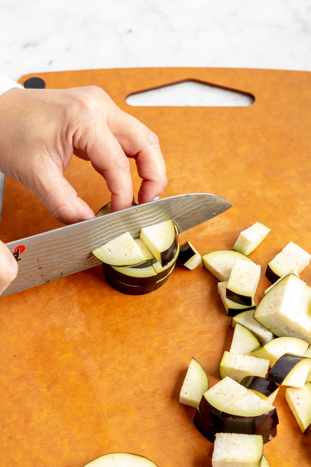Hand cubing eggplant on an epicurean cutting board.
