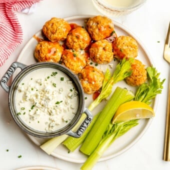 Plate of buffalo chicken meatballs with a side of blue cheese dipping sauce and celery sticks.