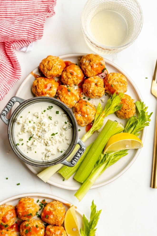 Plate of buffalo chicken meatballs with a side of blue cheese dipping sauce and celery sticks.