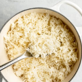 White pot with fluffy white rice in it with a silver spoon with a spoonful of rice.