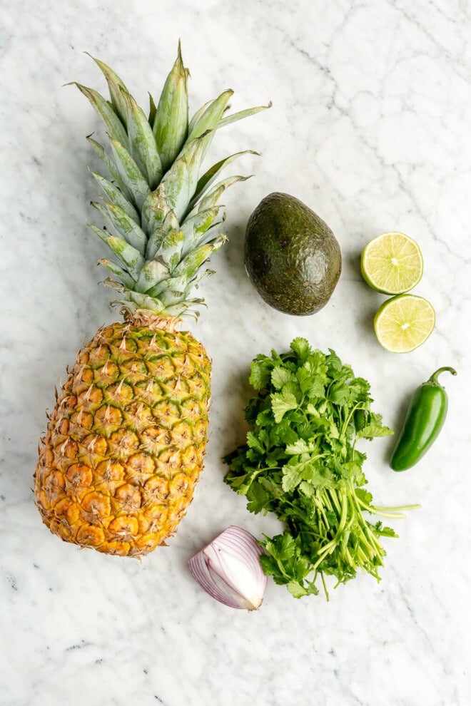 Pineapple salsa ingredients on a grey and white marble surface. 