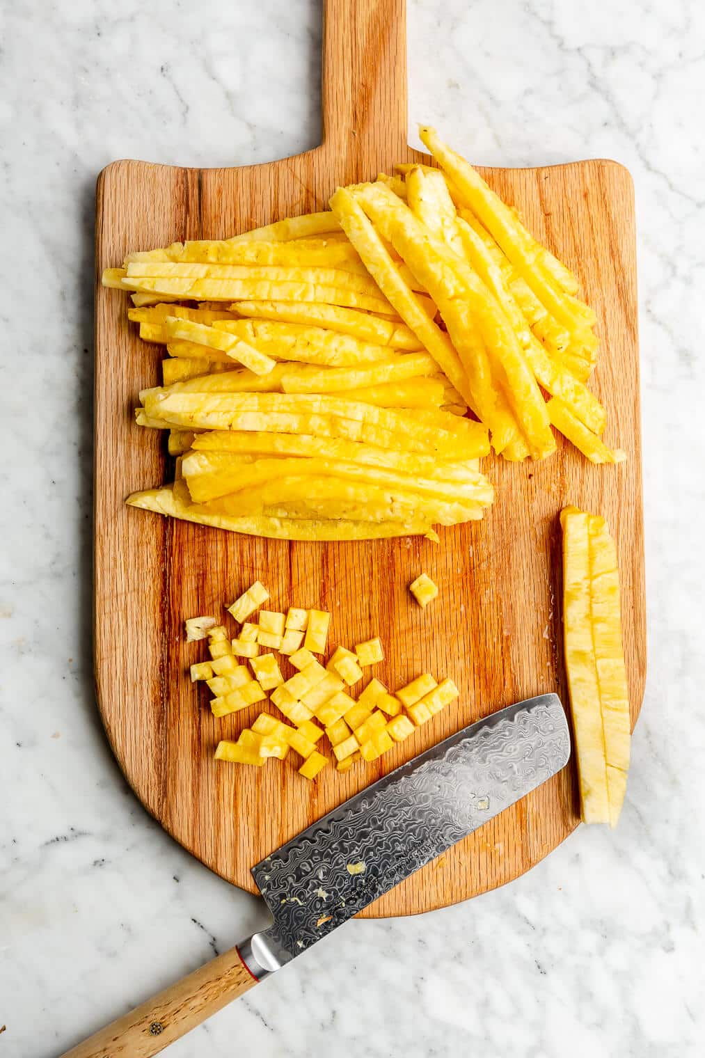 Diced and sliced pineapple on a wooden cutting board.