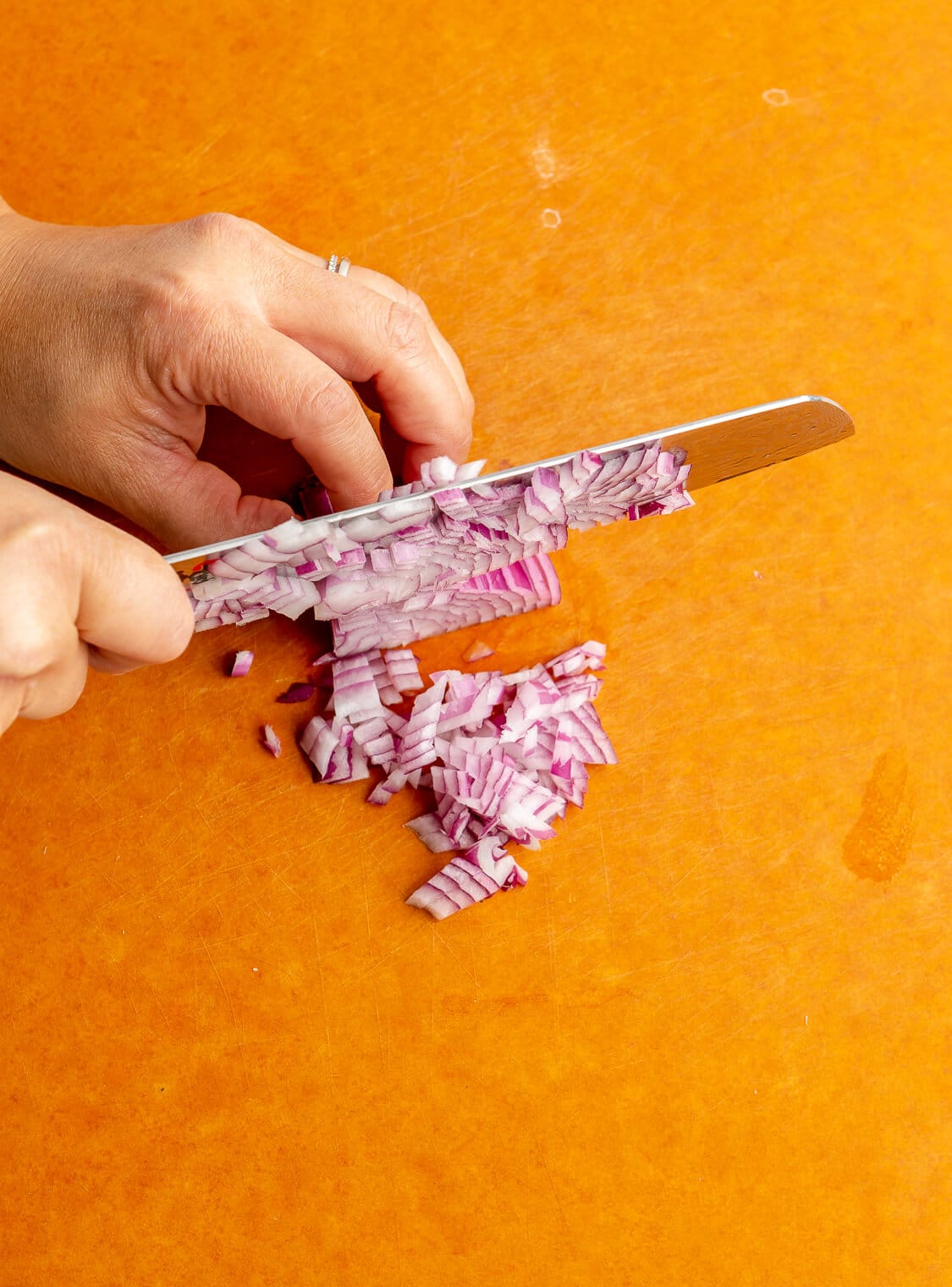 Hand holding a butcher knife dicing onions on a cutting board.