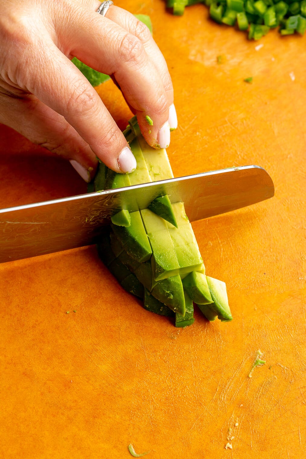 Hand holding a butcher knife dicing avocado.