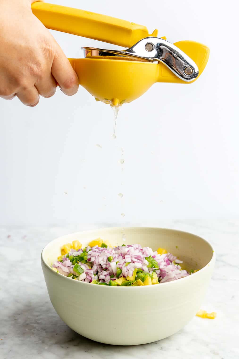 Hand holding citrus juicer squeezing juice into a bowl of pineapple salsa ingredients.