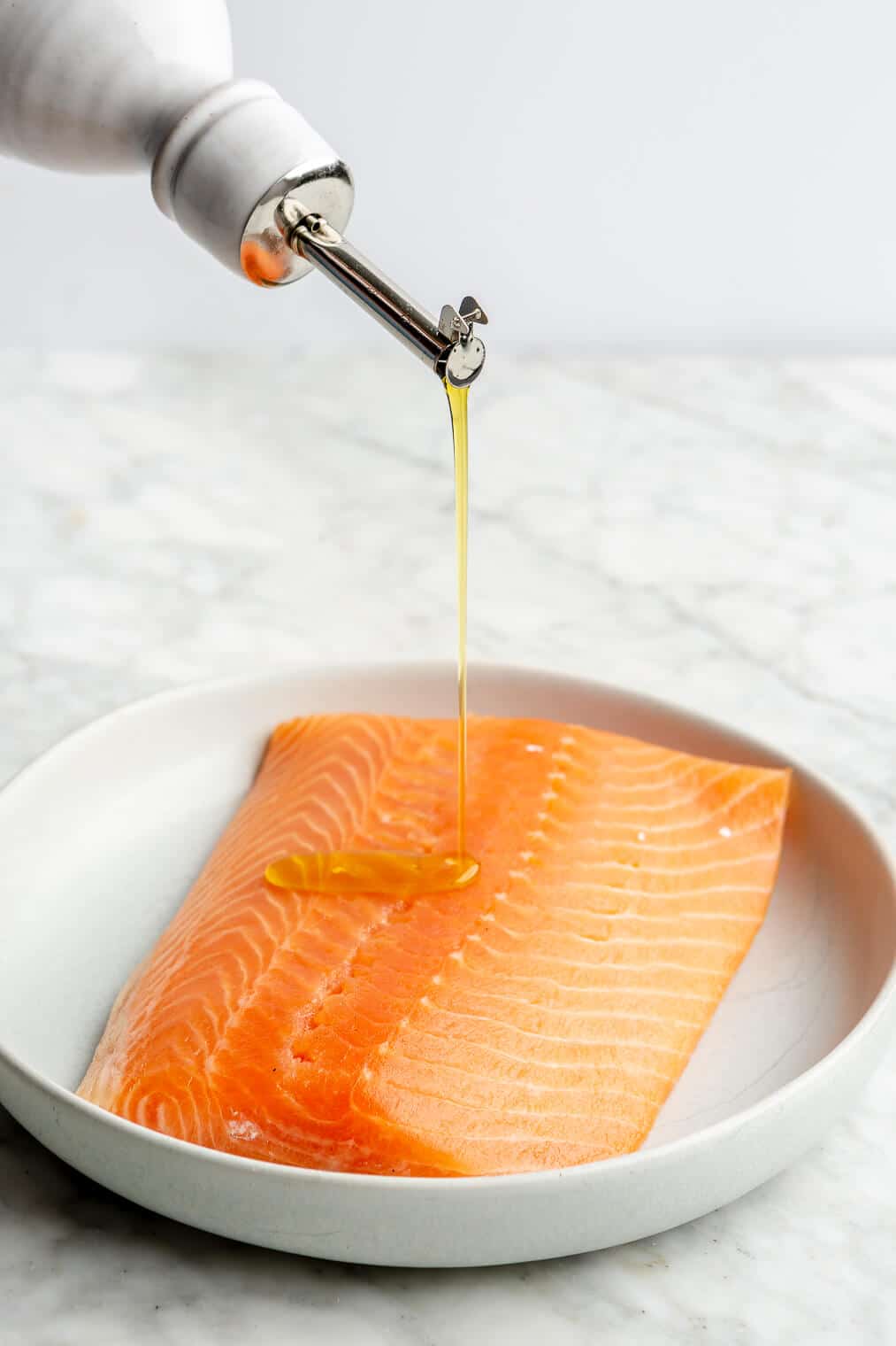 An olive oil dispenser drizzling olive oil over top a salmon filet.