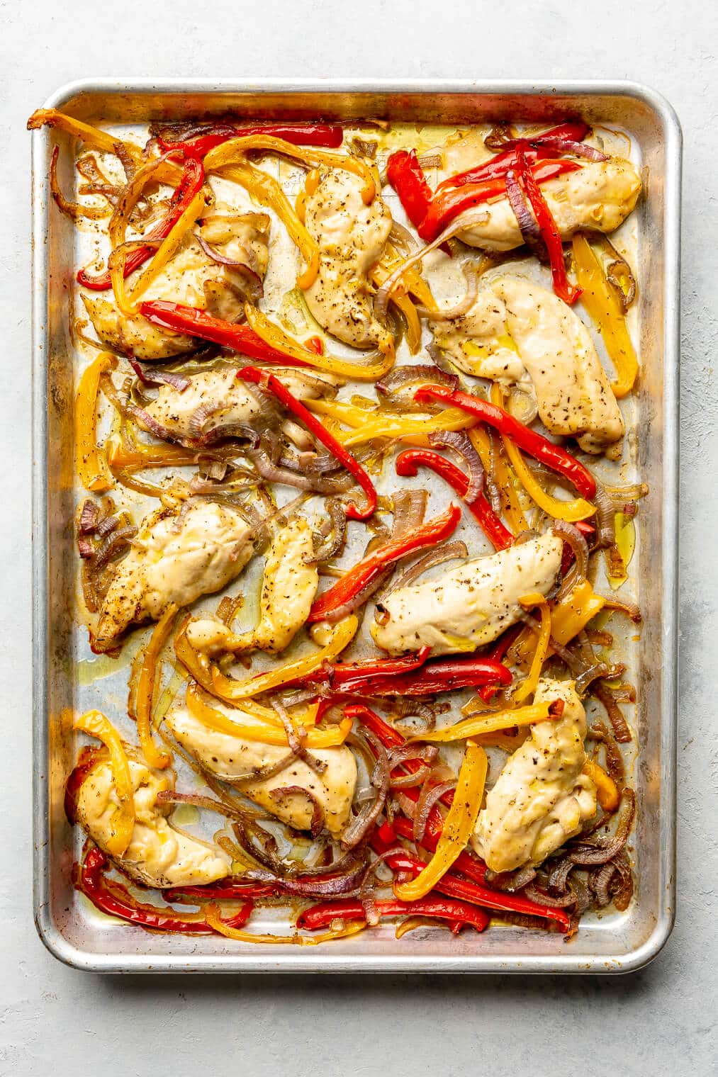 A sheet pan of cooked chicken fajitas, complete with chicken, red bell peppers, yellow bell peppers, and onions.