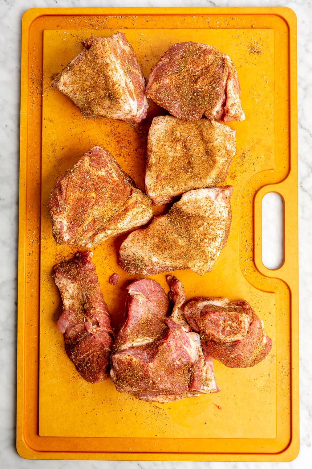 Chunks of pork shoulder on a cutting board seasoned with seasoning.