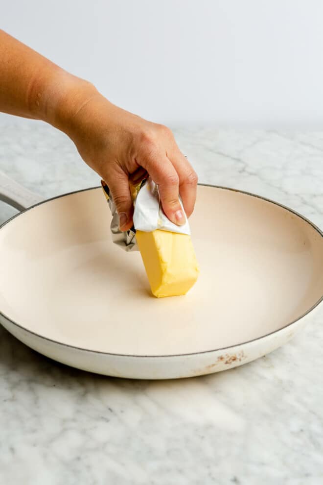 Hand holding a stick of butter, greasing a skillet.