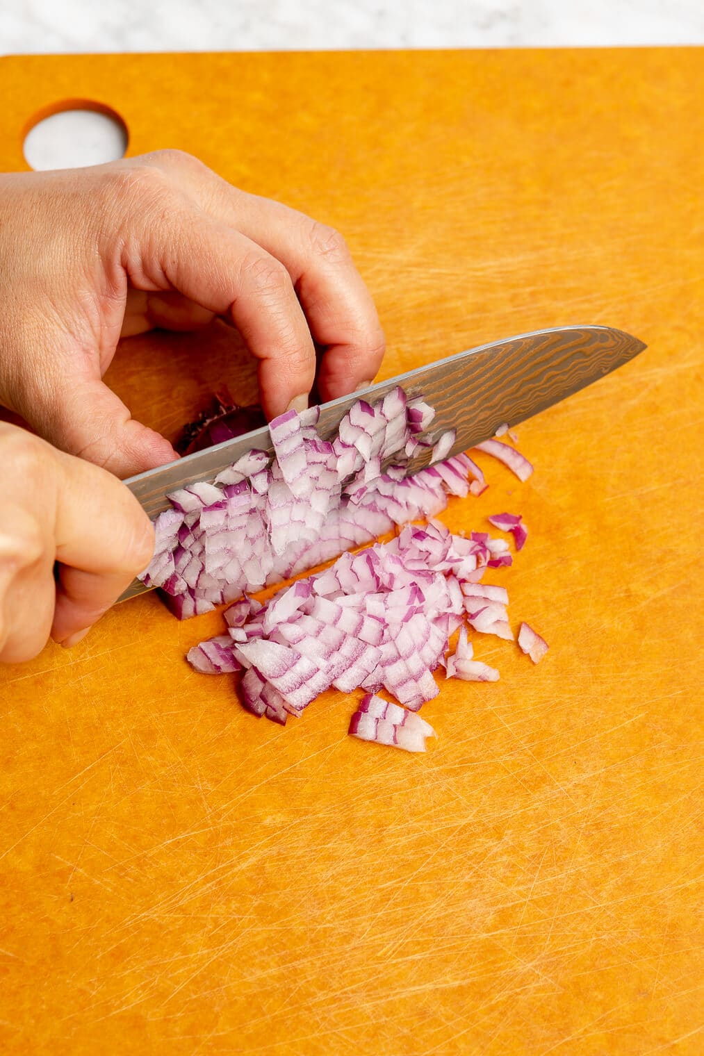 A person finely chopping a purple onion with a chef's knife on an orange cutting board.