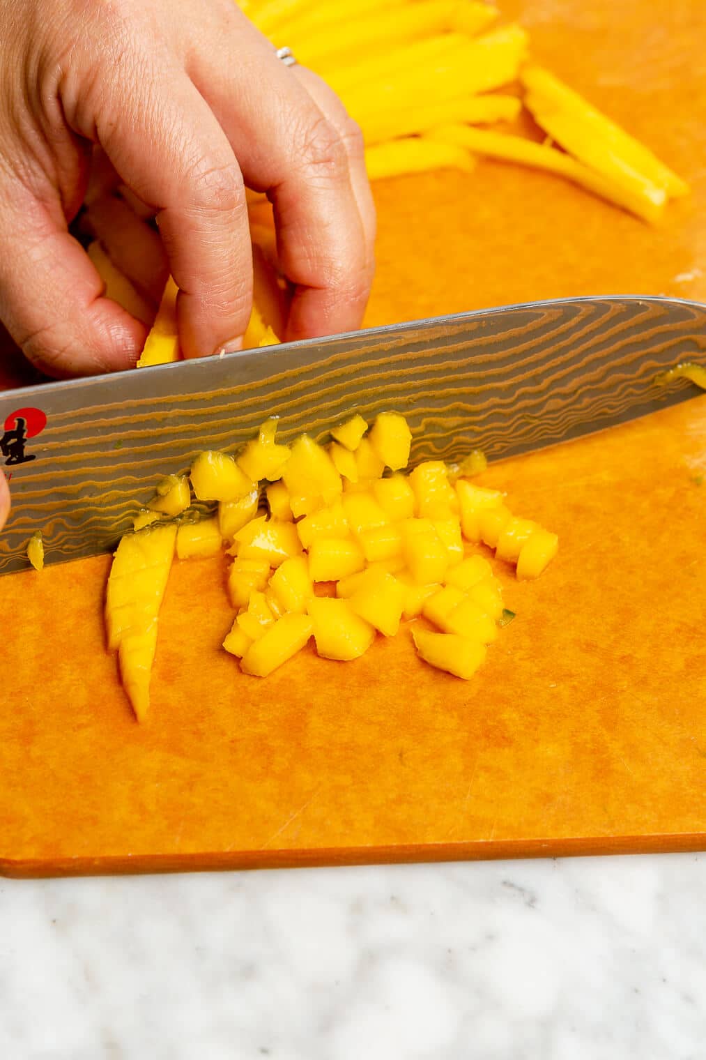 A person finely chopping a mango with a chef's knife on an orange cutting board.