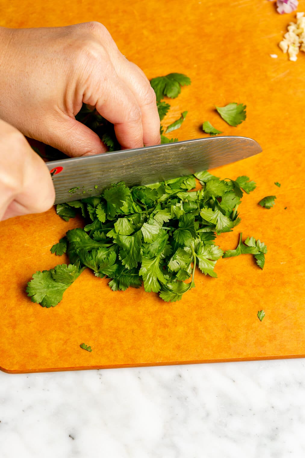 A person roughly chopping cilantro with a chef's knife on an orange cutting board.