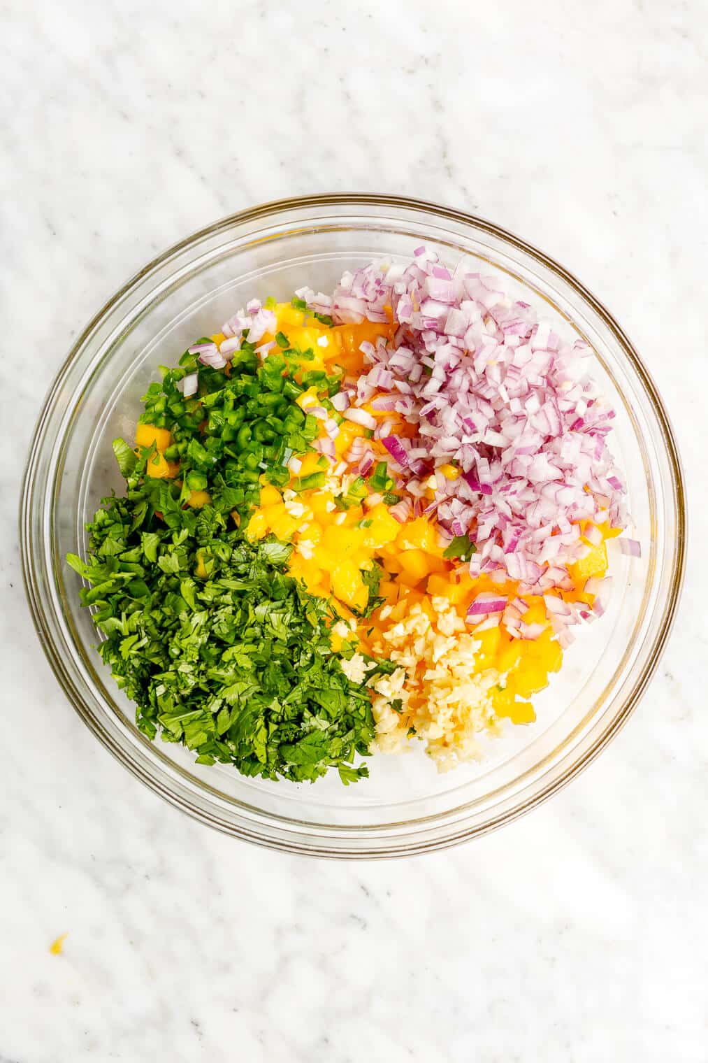 A large glass bowl of mango salsa ingredients before they're mixed.