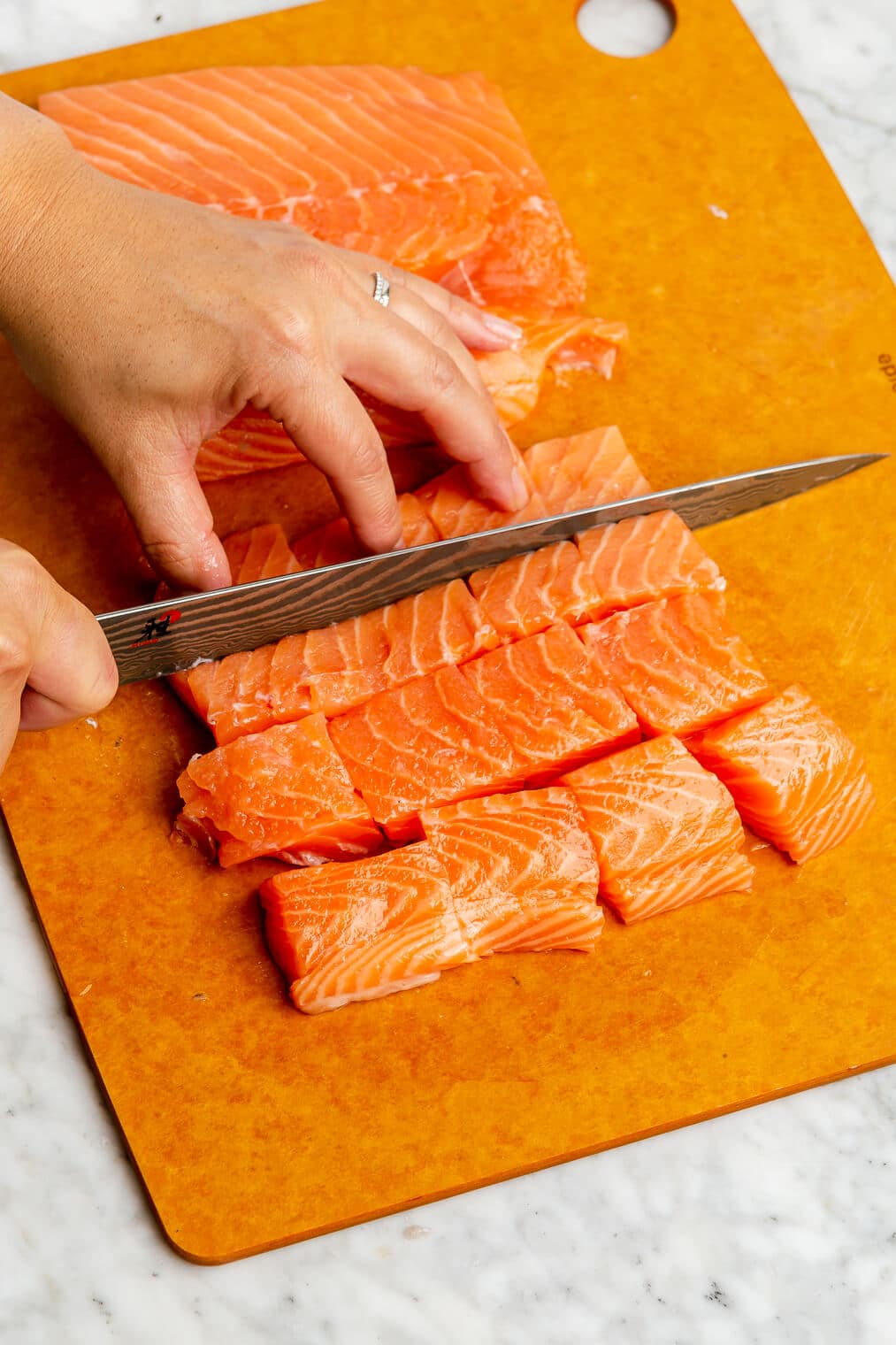 A salmon filet being cut into cubes on an orange cutting board.