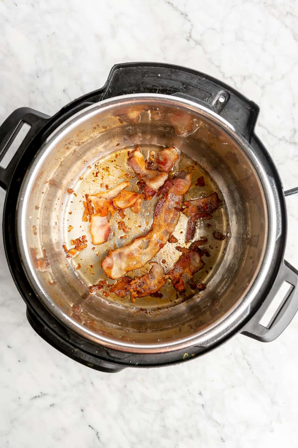 Strips of bacon cooking in the basin of an Instant Pot.