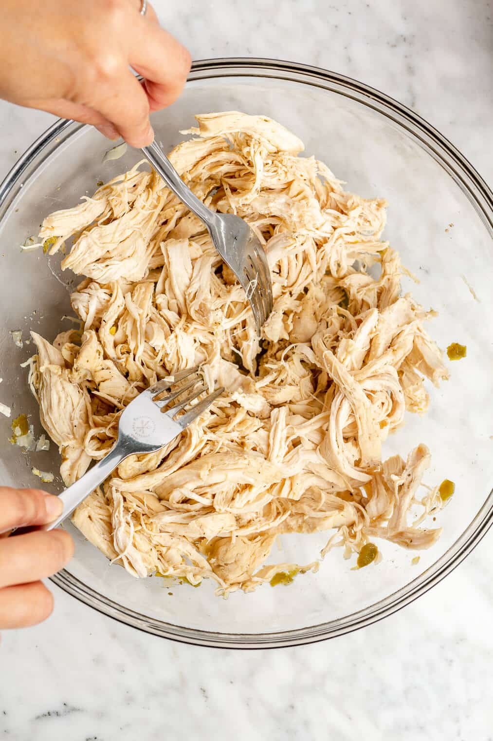 Cooked chicken breasts in a glass bowl being shredded with two forks.