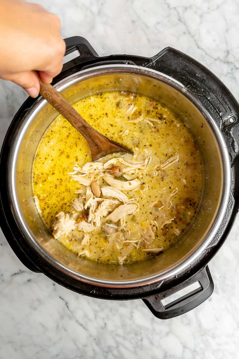A person using a wooden spoon to stir the ingredients for White Chicken Chili together in the Instant Pot.