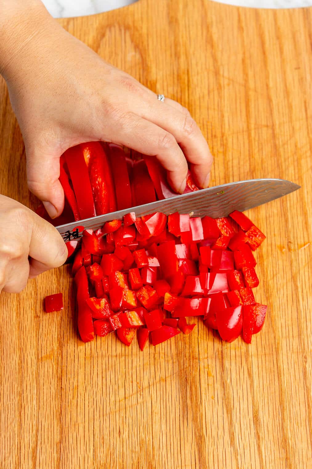 Hand dicing red peppers on a wooden cutting board.