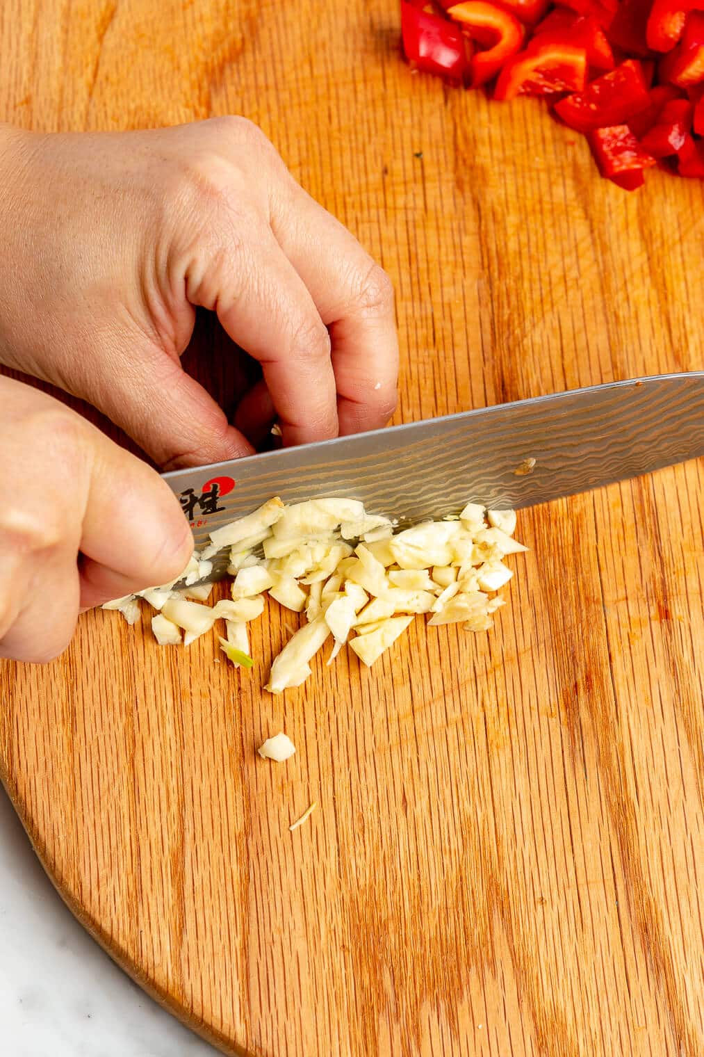 Hand mincing garlic with a chef's knife on a wooden cutting board.
