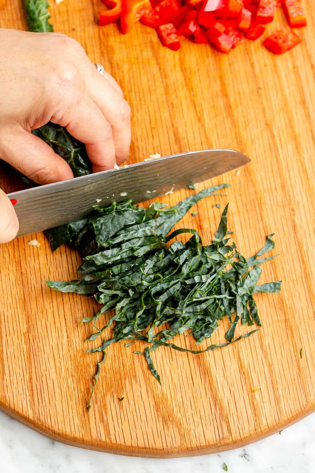 Hand shredding kale with a butcher knife on a wooden cutting board.