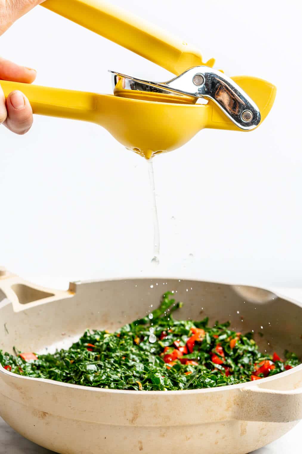 Hand squeezing a citrus juicer over top of kale and veggies in a saute pan.