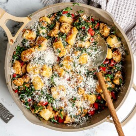 Beige pan with gnocchi, sausage, and kale garnished with parmesan cheese on a white and black marble surface.
