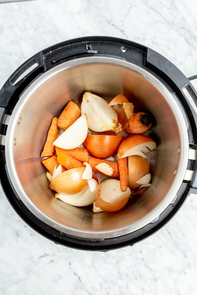 Chopped onions, carrots, and garlic in the pot of an Instant Pot.