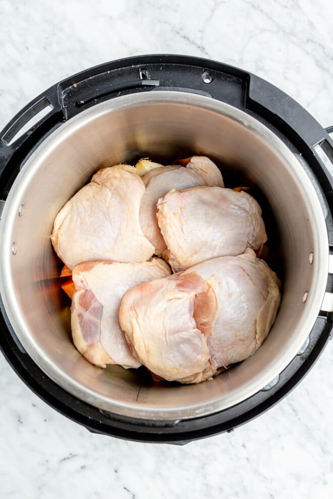 Bone-in chicken thighs sitting in the pot of an Instant Pot on top of chopped onions and carrots.