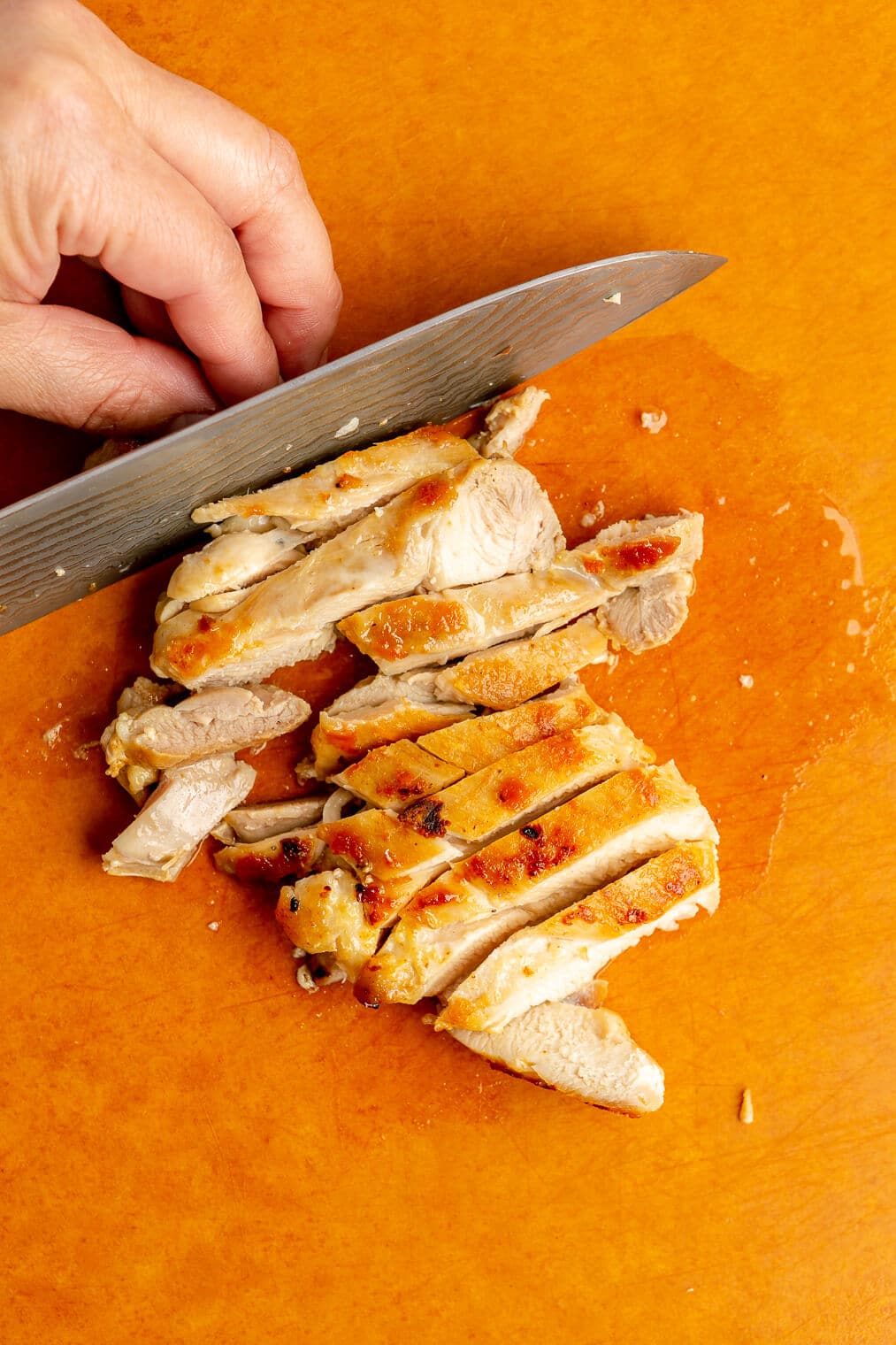 Hand slicing chicken on a cutting board