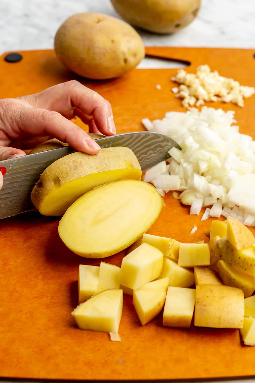 a person cutting potatoes on an orange cutting board next to chopped onion and minced garlic
