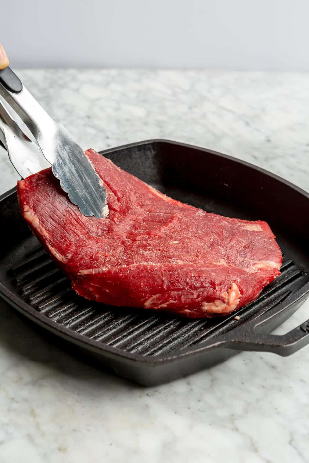 A flank steak being seared on a cast iron sear pan.