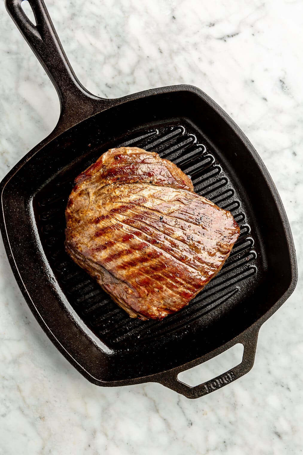 A flank steak being seared on a cast iron sear pan.