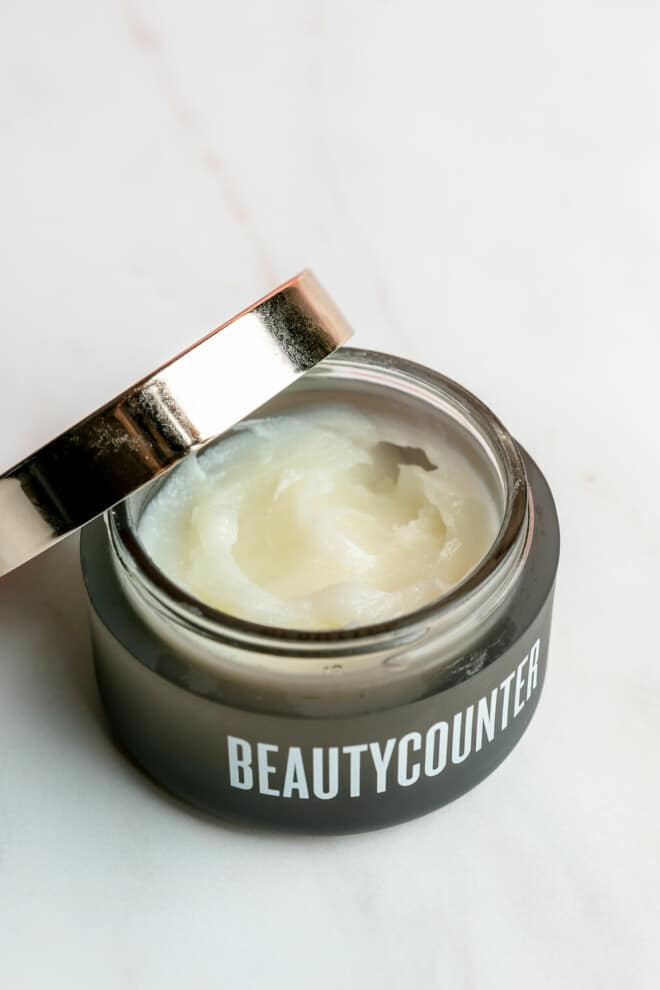 An open jar of Beautycounter's cleansing balm sitting on a marble surface.