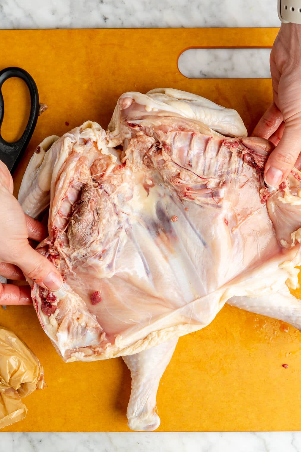 A raw whole chicken with the spine cut out on a large orange cutting board.