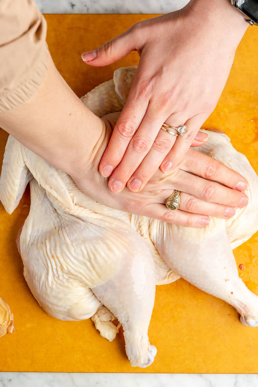A person using their hands to press down on a chicken to spatchcock it.